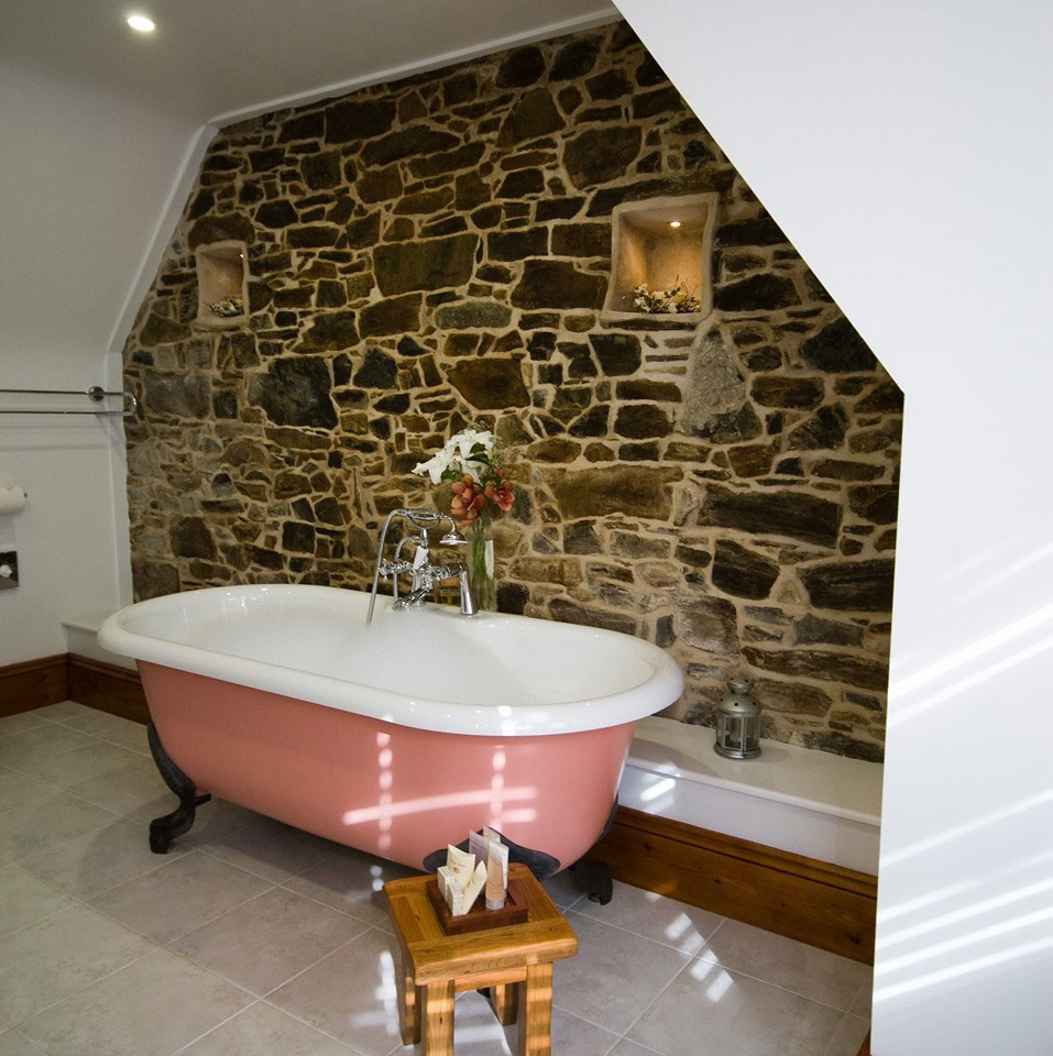 Style Plumbing & Heating roll top bath with exposed natural stone wall